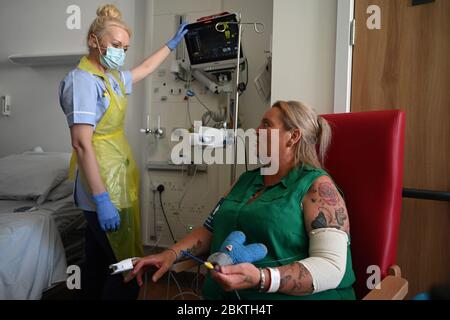 Un membre du personnel clinique porte un équipement de protection individuelle (EPI) pour s'en prendre à la patiente Trudy Woodfall qui se remet du coronavirus dans le service de récupération Covid de l'hôpital Royal Papworth de Cambridge. Banque D'Images