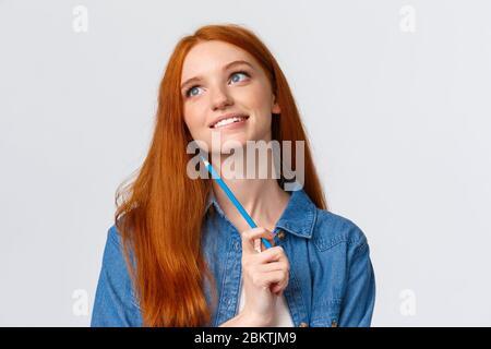 Belle et créative, pensive rêveuse souriante femme à la tête rouge regardant et penser, l'imagerie quelque chose de beau, tenant le crayon coloré, dessin Banque D'Images