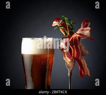 Verre de bière et tranches de bacon frit savoureux garni de romarin. Banque D'Images
