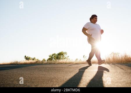 Femme en surpoids sur la course matinale sur la route. Plus de taille femme s'exerçant le matin. Banque D'Images