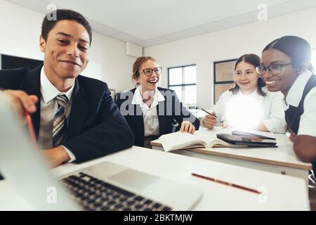 Groupe d'étudiants étudiant ensemble sur un ordinateur portable en classe. Garçons et filles en uniforme travaillant sur une affectation scolaire. Banque D'Images