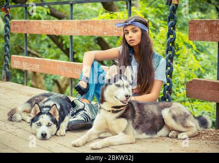 Jolie fille et ses animaux de compagnie. Nachez la femme de rapaper avec ses chiens husky, isolé parc vert arrière-plan assis sur le pont les trois regardant vous caméra. Tak Banque D'Images