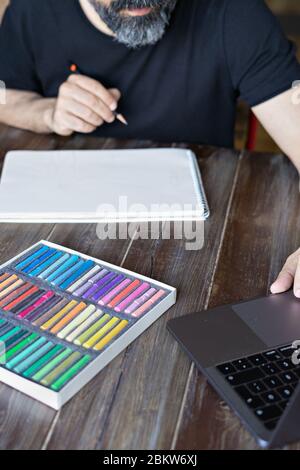 personne apprenant la peinture avec le crayon et le pastel craie sur papier devant l'ordinateur portable, table en bois. Verticale Banque D'Images