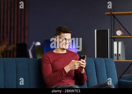 Jeune freelance avec smartphone et sourire. Heureux homme utilisant m Banque D'Images