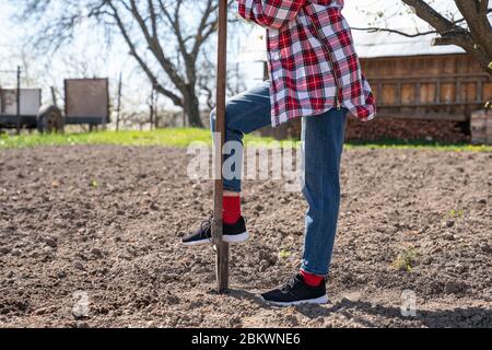 Photo courte d'une jeune femme en chemise à carreaux et jeans qui tient une pelle tout en travaillant dans le jardin Banque D'Images