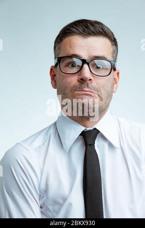 Jeune homme d'affaires en lunettes et chemise blanche avec cravate noire, avec drôle d'expression de visage découragé, en tournant sa bouche et en regardant la caméra avec sur Banque D'Images