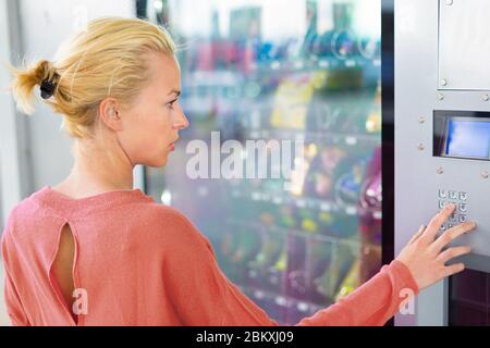 Femme caucasienne utilisant un distributeur automatique moderne. Sa main droite est placée sur le coussin DIA Banque D'Images