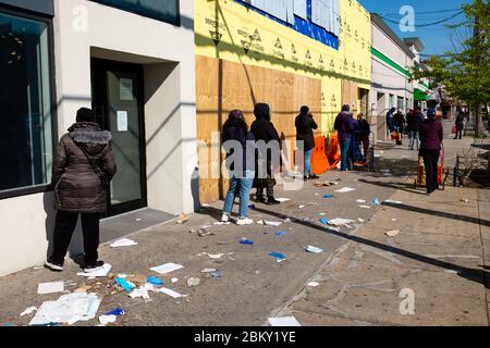 Brooklyn, NY - 17 avril 2020. Les clients forment une ligne au milieu d'une dérive de gants chirurgicaux jetés et d'autres déchets à l'extérieur d'un magasin Dollar Tree, avec le gre Banque D'Images