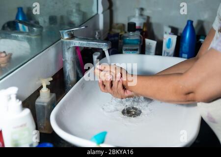 Un adulte se lavant correctement les mains et les bras avec du savon à l'alcool sous l'évier/lavabo des toilettes pour combattre le coronavirus. Banque D'Images