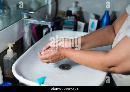 Un adulte se lavant correctement les mains et les bras avec du savon à l'alcool sous l'évier/lavabo des toilettes pour combattre le coronavirus. Banque D'Images