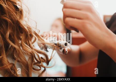 Cheveux bouclés, femme avec cheveux longs blond ondulé repassage, utilisation du fer à friser, boucleur pour des boucles parfaites Banque D'Images