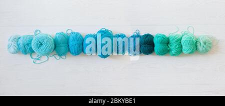 Fils pour tricoter les couleurs bleu-vert, vert et turquoise. Fond long en bois blanc Banque D'Images