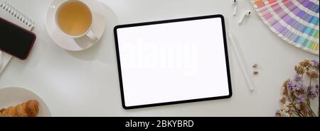 Vue de dessus d'une table de travail minimaliste avec tablette maquette, fournitures de créateur et repas de petit déjeuner sur table de travail blanche Banque D'Images
