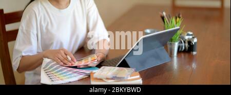 Photo rognée d'une étudiante de l'université travaillant sur son projet et choisissant la couleur sur la nuance de couleur sur la table de travail en bois Banque D'Images