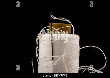 Aiguille et coton blanc, fil emmêlé sur rouleau pour la couture. Fils utilisés dans l'industrie textile et textile. Fond noir Banque D'Images