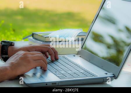 Personne qui travaille ou apprend en ligne par ordinateur portable sur le bureau dans le jardin de la maison. Banque D'Images