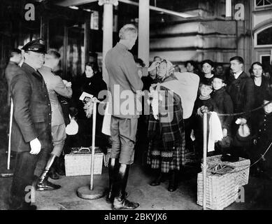 Les agents des services de santé publique examinent les immigrants arrivant à Ellis Island en 1918 pendant la pandémie de grippe espagnole. Banque D'Images