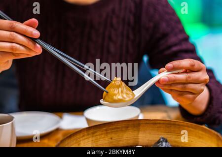 Une dame chinoise ramasse une soupe de xiaolongbao gourmet au foie gras en utilisant des baguettes et une cuillère. Banque D'Images