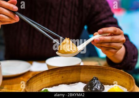 Une dame chinoise ramasse une soupe de xiaolongbao gourmet au foie gras en utilisant des baguettes et une cuillère. Banque D'Images