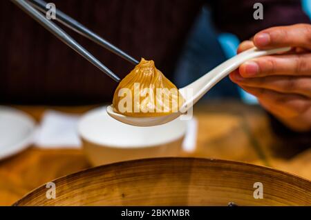 Une dame chinoise ramasse une soupe de xiaolongbao gourmet au foie gras en utilisant des baguettes et une cuillère. Banque D'Images