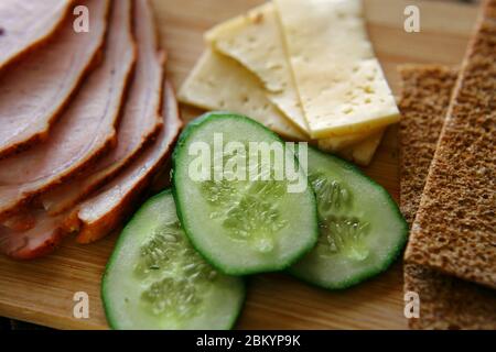 Trancher du jambon, des concombres et du fromage avec des pains fins et grossiers se trouvent sur une planche en bois. Banque D'Images