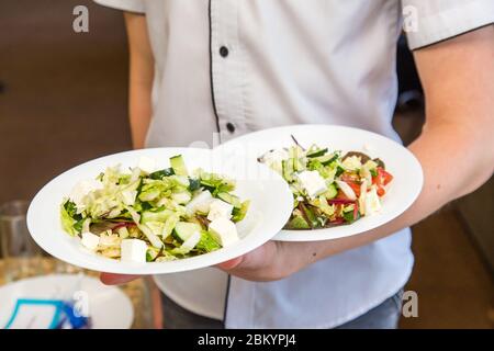 Le serveur tient deux assiettes de salade, travaille sur le service d'événement. Banque D'Images