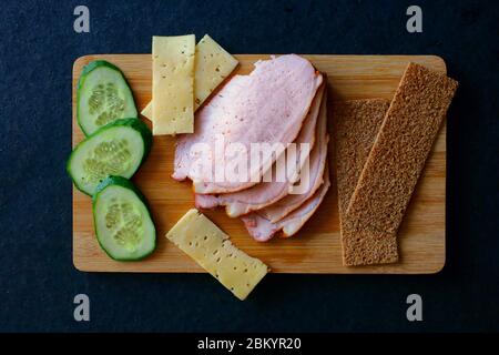 Trancher du jambon de viande, des concombres, du fromage et des pains à la gouvernail sur une planche en bois. Vue de dessus Banque D'Images