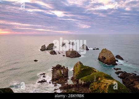 Vue sur les formations rocheuses qui donnent au point de Nugget son nom au lever du soleil par une journée nuageux et une mer calme. Banque D'Images