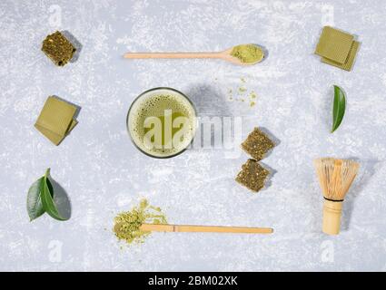 Disposition de la table de thé matcha, cuillères en bois avec poudre de matcha, fouet, feuilles, chocolat, barre de céréales sur fond texturé gris clair. K Banque D'Images