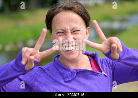 Une femme hispanique d'âge moyen enthousiaste avec un sourire sympathique et sympathique donnant un double V-signe d'approbation et de succès en plein air au printemps Banque D'Images