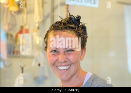 Une femme heureuse avec de la teinture sur ses cheveux debout dans sa salle de bains à la maison se tournant pour regarder la caméra dans un gros plan de tête Banque D'Images
