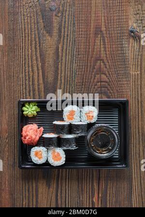 petits pains à sushis au saumon dans une boîte en plastique sur une table en bois, vue du dessus, livraison de nourriture Banque D'Images