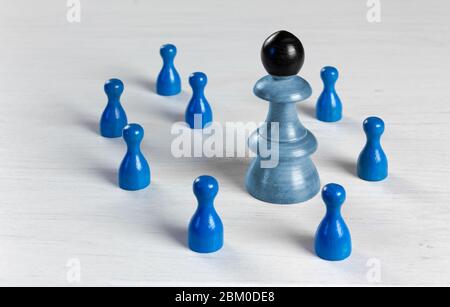 Un gros pion à tête noire entouré de petits pions sur une table en bois blanc Banque D'Images