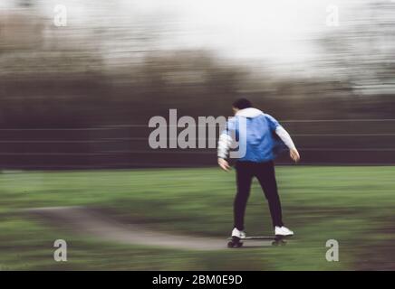 Vue arrière d'un homme flou et méconnu dans des vêtements de sport, qui se prompt sur une planche à roulettes le long d'une route vallonnée, en train de faire une cascade dans un parc de skate Banque D'Images