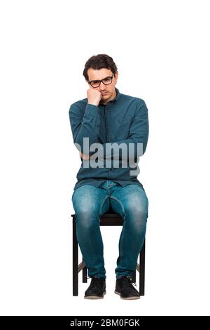 Toute la longueur d'un homme d'affaires agacé garde la main sous la joue, assis sur une chaise isolée sur fond blanc. Travailleur d'affaires, porte des lunettes, attentif Banque D'Images