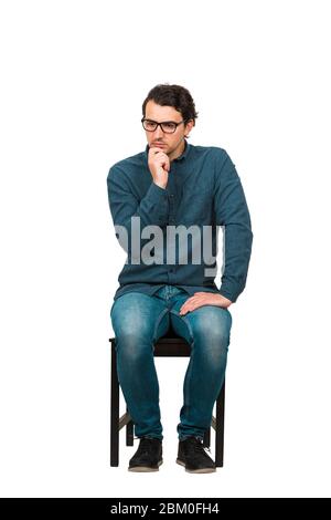 Toute la longueur d'homme d'affaires attentionné garde la main sous le menton, assis sur une chaise isolée sur fond blanc. Employé d'affaires, porte des lunettes, regardant Banque D'Images
