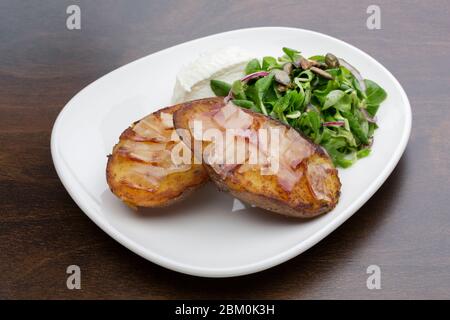 Pommes de terre cuites au four avec bacon, fromage frais et salade sur une table en bois, dans une assiette en céramique Banque D'Images