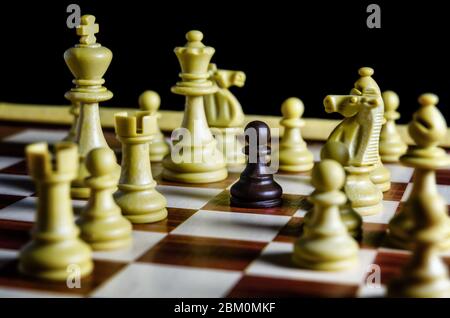 Pion noir sur un échiquier seul contre toutes les pièces blanches Banque D'Images