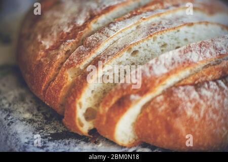 Un pain frais de farine de blé, coupé en morceaux, repose sur une plaque de cuisson parsemée de farine friable. Boulangerie. Gâteau fait maison. Banque D'Images