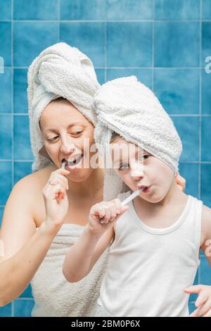 Une femme et un garçon avec des serviettes sur la tête se brossant les dents. Banque D'Images