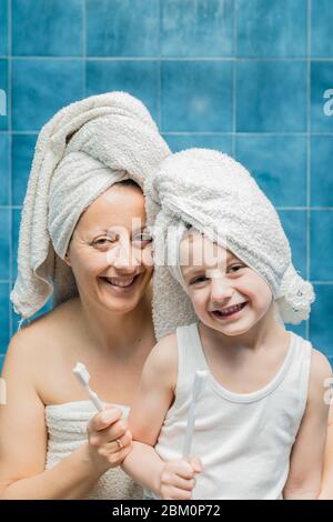 Une femme et un garçon avec des serviettes sur la tête se brossant les dents. Banque D'Images