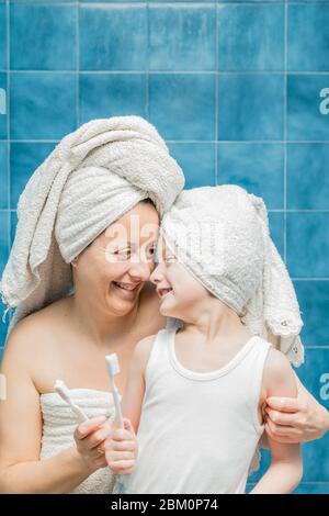 Une femme et un garçon avec des serviettes sur la tête se brossant les dents. Banque D'Images