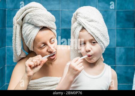 Une femme et un garçon avec des serviettes sur la tête se brossant les dents. Banque D'Images