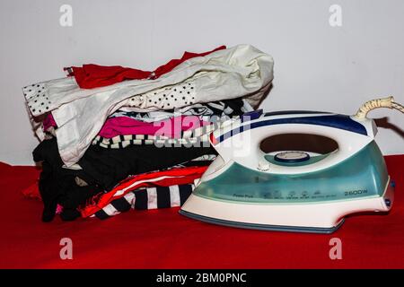 Pile de vêtements en coton coloré et fer à repasser. Linge de maison repassage isolé. Banque D'Images