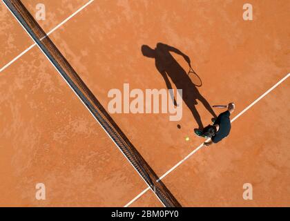 Longue ombre d'un joueur de tennis sur un terrain de terre de tennis Banque D'Images