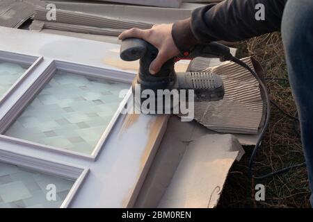 master traite les portes en bois avec un outil de meulage, restauration, préparation de la porte pour la peinture, nettoyage de la surface du bois. Banque D'Images