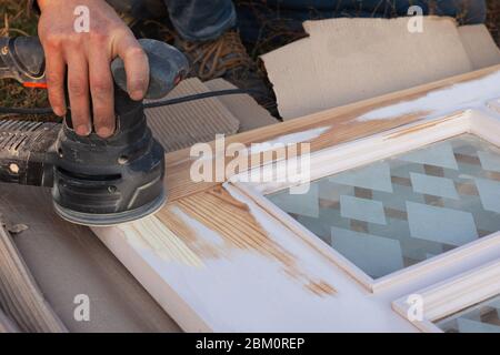 master traite les portes en bois avec un outil de meulage, restauration, préparation de la porte pour la peinture, nettoyage de la surface du bois. Banque D'Images