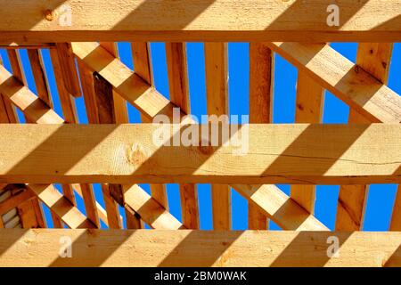 Une vue abstraite des poutres et de la charpente du toit en bois sous forme de construction en cours contre un ciel bleu. Banque D'Images