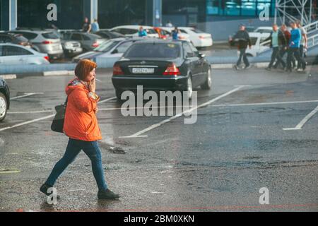 Moscou, Russie - 2 MAI 2018 : une femme en veste rouge descend une rue humide et fume une cigarette dans un lieu public Banque D'Images