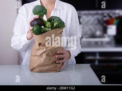 Femme caucasienne tenant sac de papier brun plein de légumes verts. Banque D'Images